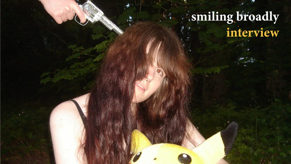 Hazel of smiling broadly sits, holding a Pikachu plush. Someone is pointing a gun to her head from just off-screen.